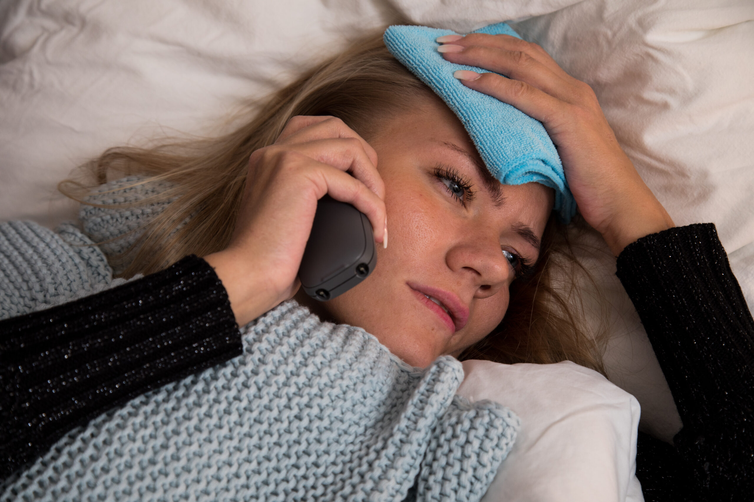 Eine Frau liegt krank im Bett und telefoniert.