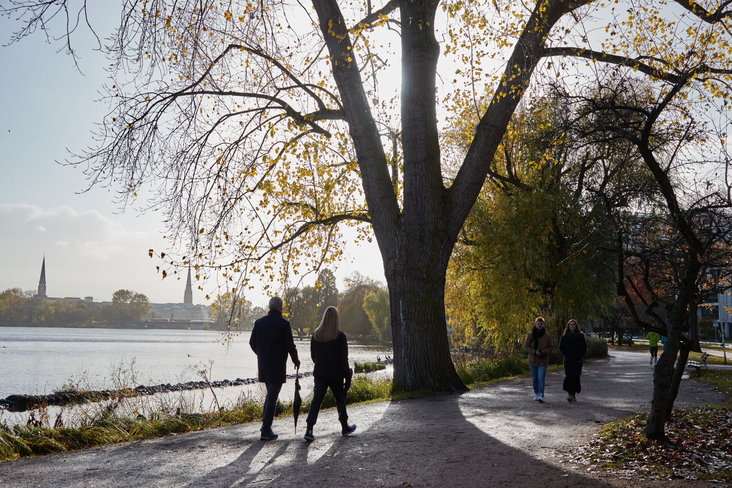 Spaziergänger mit zusammengefaltetem Regenschirm gehen an der Außenalster spazieren.