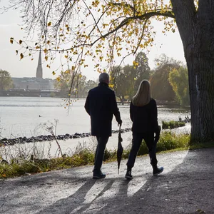 Spaziergänger mit zusammengefaltetem Regenschirm gehen an der Außenalster spazieren.