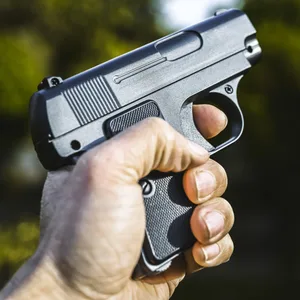 Eine Hand hält eine Schusswaffe. Der Zeigefinger ist am Auslöser.