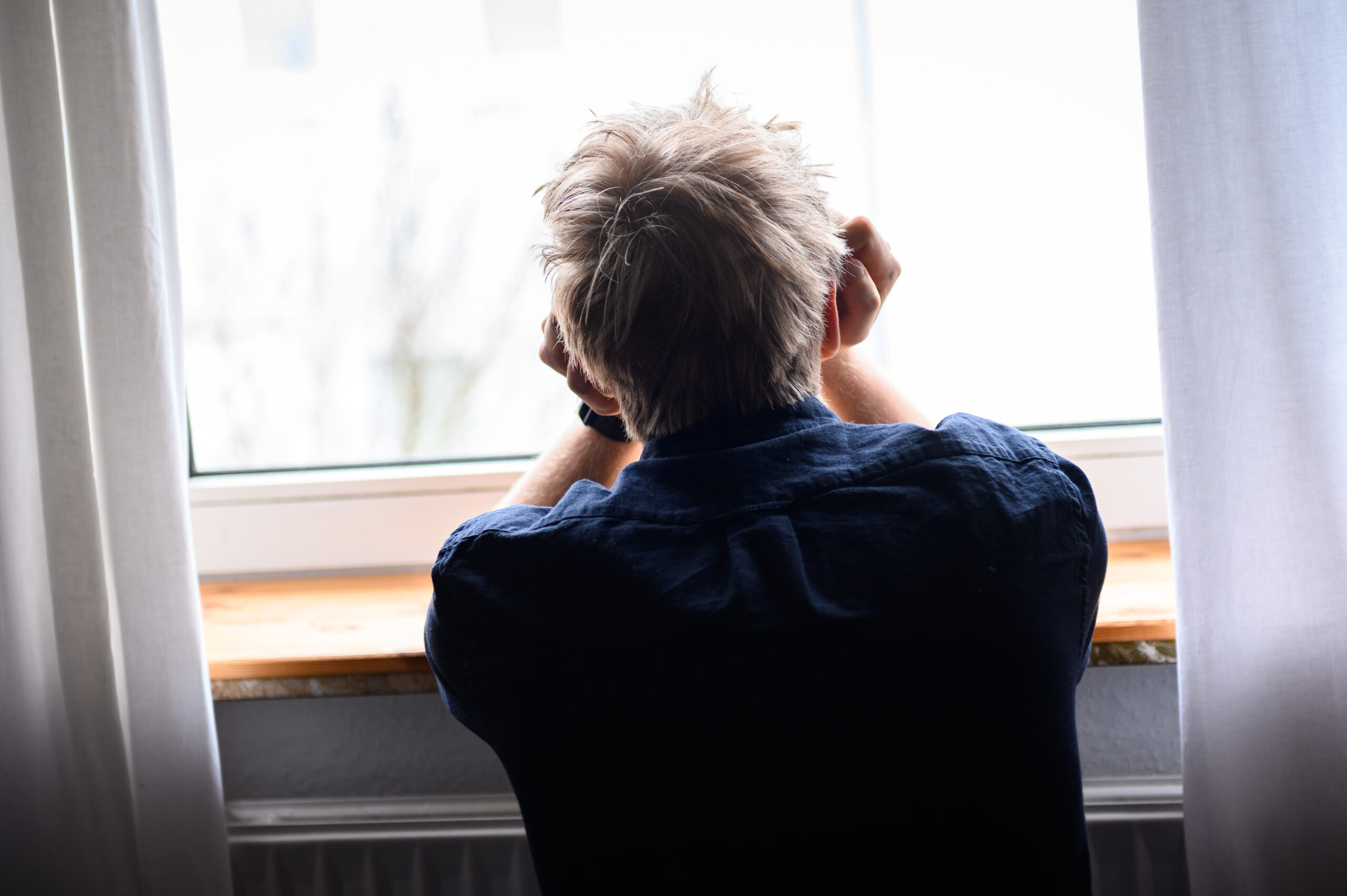 Ein Mann sitzt mit Kopf in den Händen am Fenster.