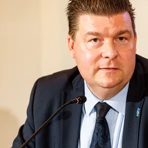 Mann im Anzug mit dunklen Haaren vor Mikro