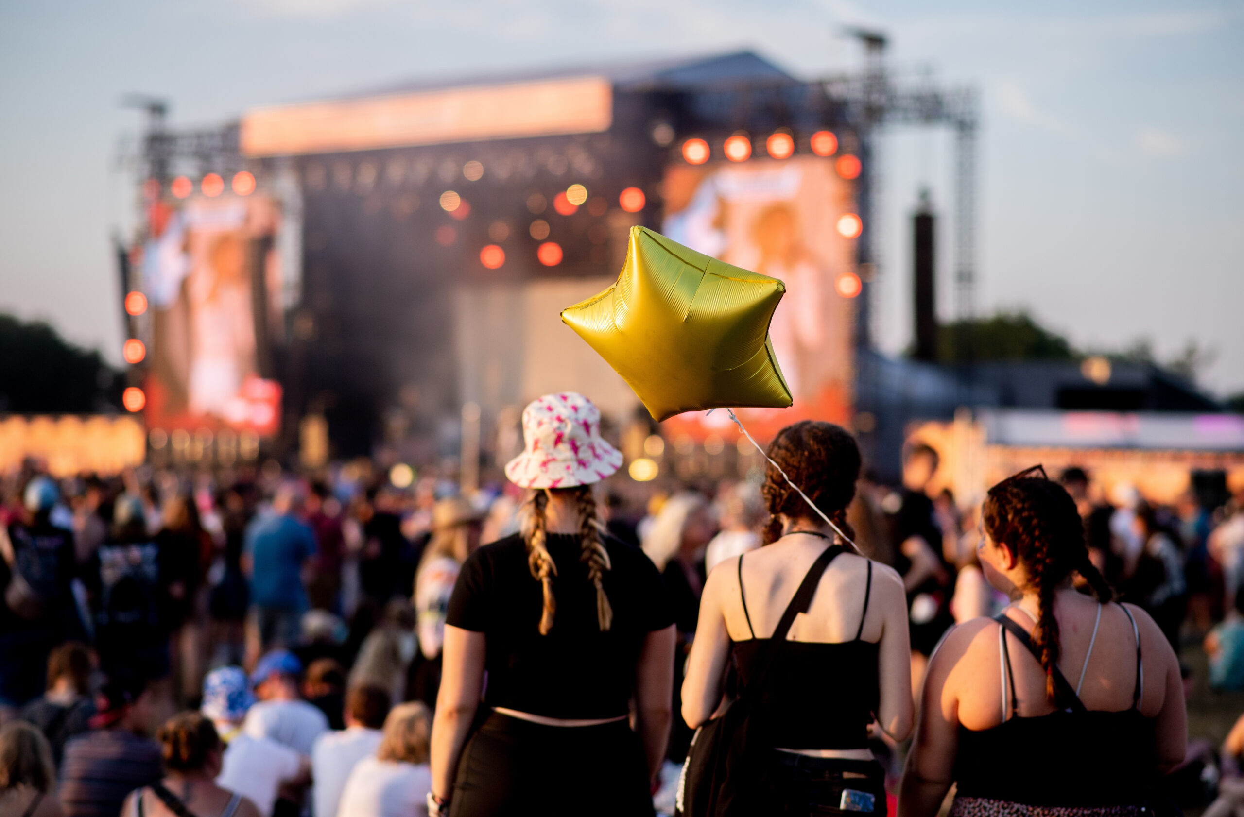 Drei junge Frauen mit Luftballon von hinten zu sehen vor einer Bühne