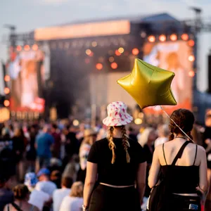 Drei junge Frauen mit Luftballon von hinten zu sehen vor einer Bühne