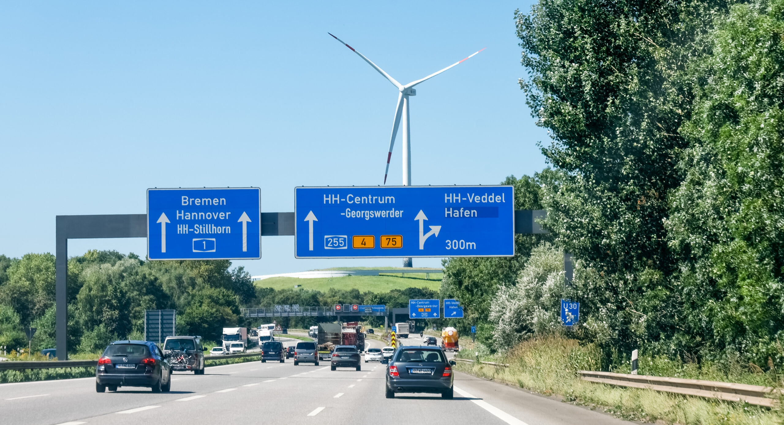 Autos fahren auf der A1 Richtung Hamburg. Über ihnen: ein Schild mit Richtungs-/Abfahrtsinformationen.