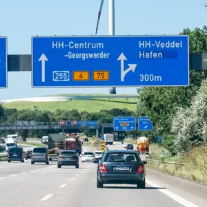 Autos fahren auf der A1 Richtung Hamburg. Über ihnen: ein Schild mit Richtungs-/Abfahrtsinformationen.