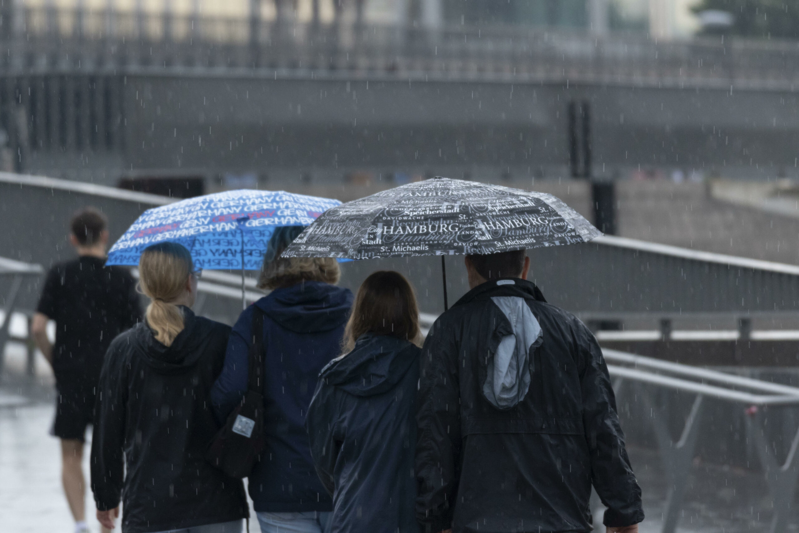 Touristen mit Regenschirmen unterwegs im Regen an den Landungsbrücken im Hafen von Hamburg.