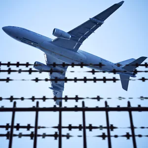 Ein Flugzeug fliegt über einen Stacheldraht hinweg.