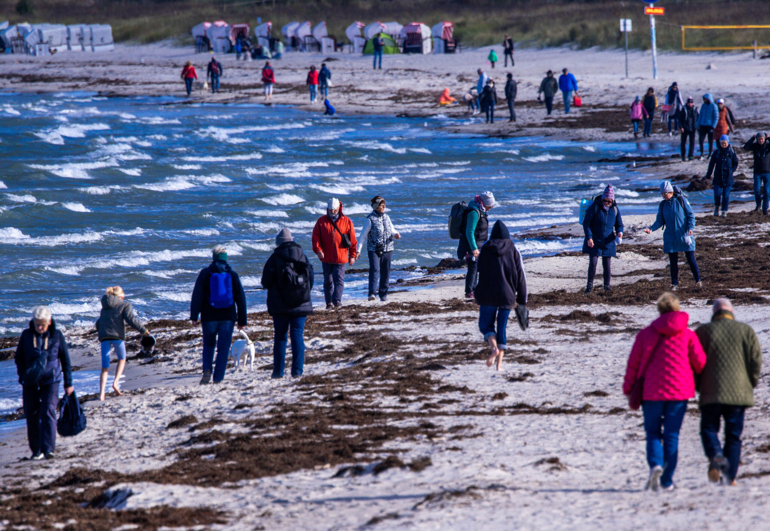 Touristen laufen in dicken Jacken an einem Ostseestrand entlang.