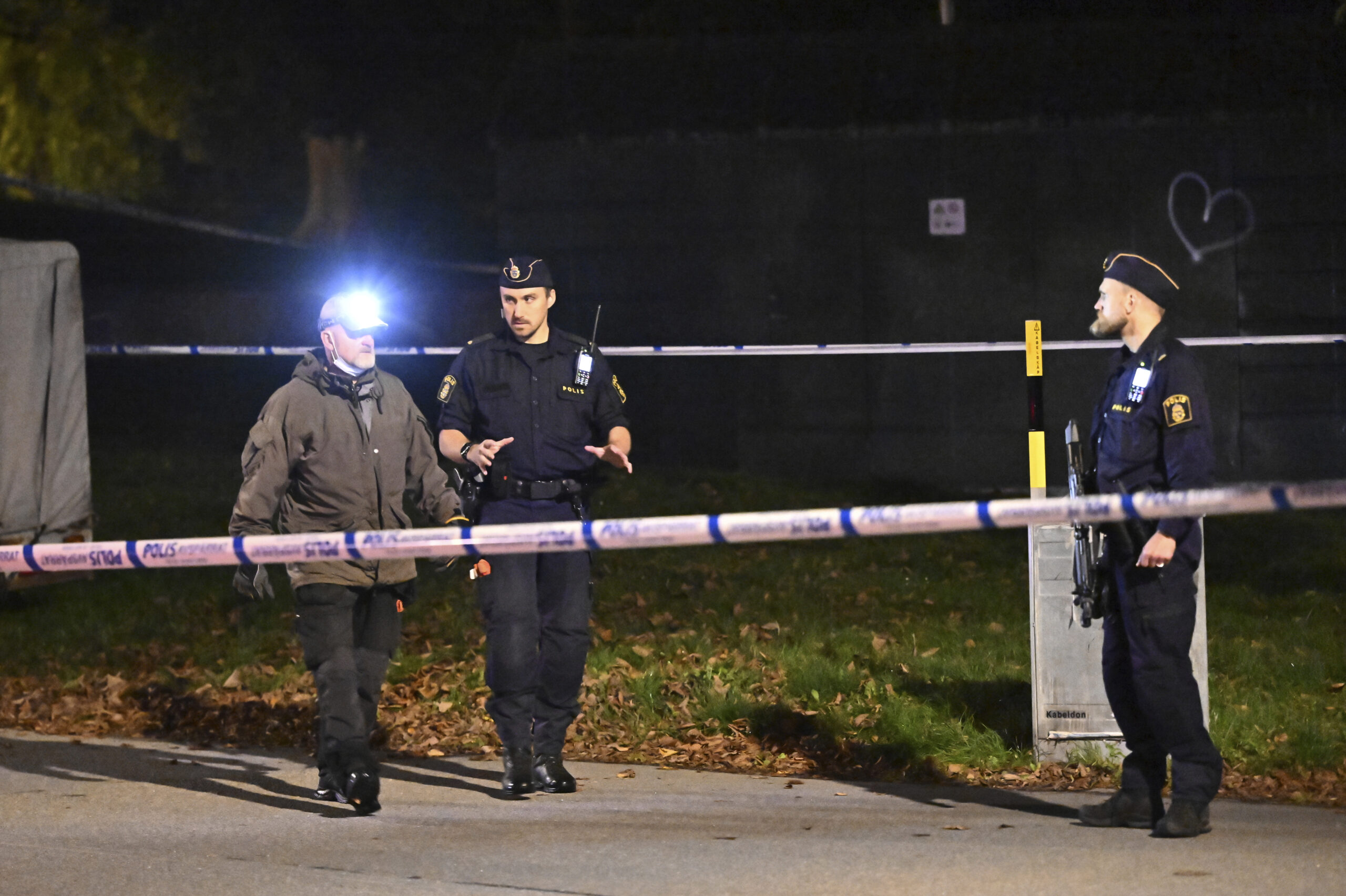 Die schwedische Polizei steht bei Nacht hinter einem Absperrband.