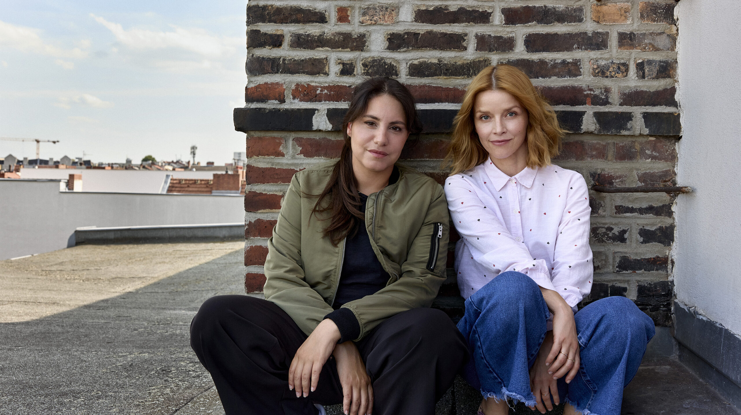 Das Foto zeigt das neue „Tatort“-Duo Almila Bagriacik (links) und Karoline Schuch (rechts). Die beiden sitzen am Hafen und schauen frontal in die Kamera