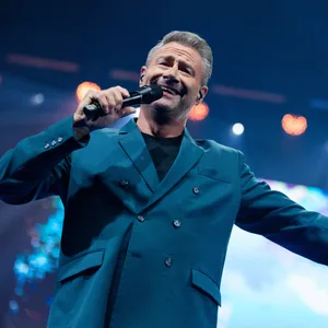Sänger Sascha singt bei der Pressekonferenz zum Auftakt von der neuen Show „Horizons“ von „Holiday on ice“. Im Hintergrund sind Scheinwerfer zu sehen. Sascha trägt einen bläulichen Anzug