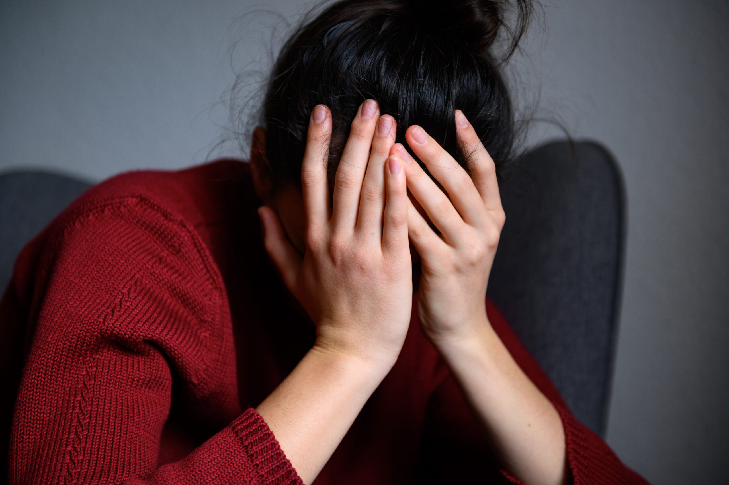 Eine Frau mit dunklen Haaren hat das Gesicht in ihren Händen vergraben