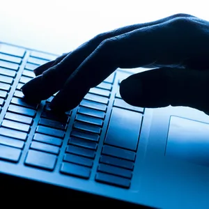 Man sieht eine Hand, die auf einer Laptop-Tastatur tippt