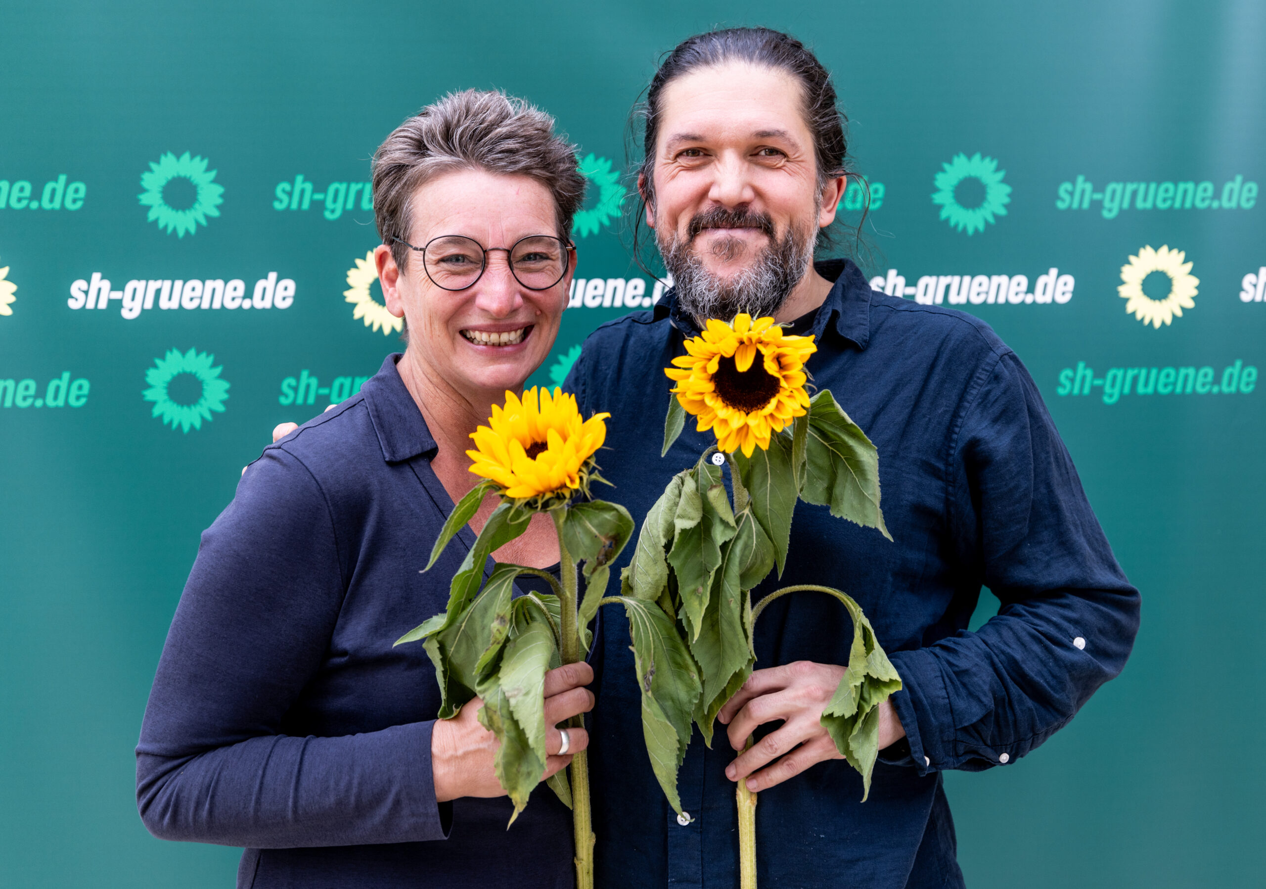 Anke Erdmann (Bündnis90/Die Grünen) und Gazi Freitag (Bündnis90/Die Grünen), halten Sonnenblumen in den Händen.