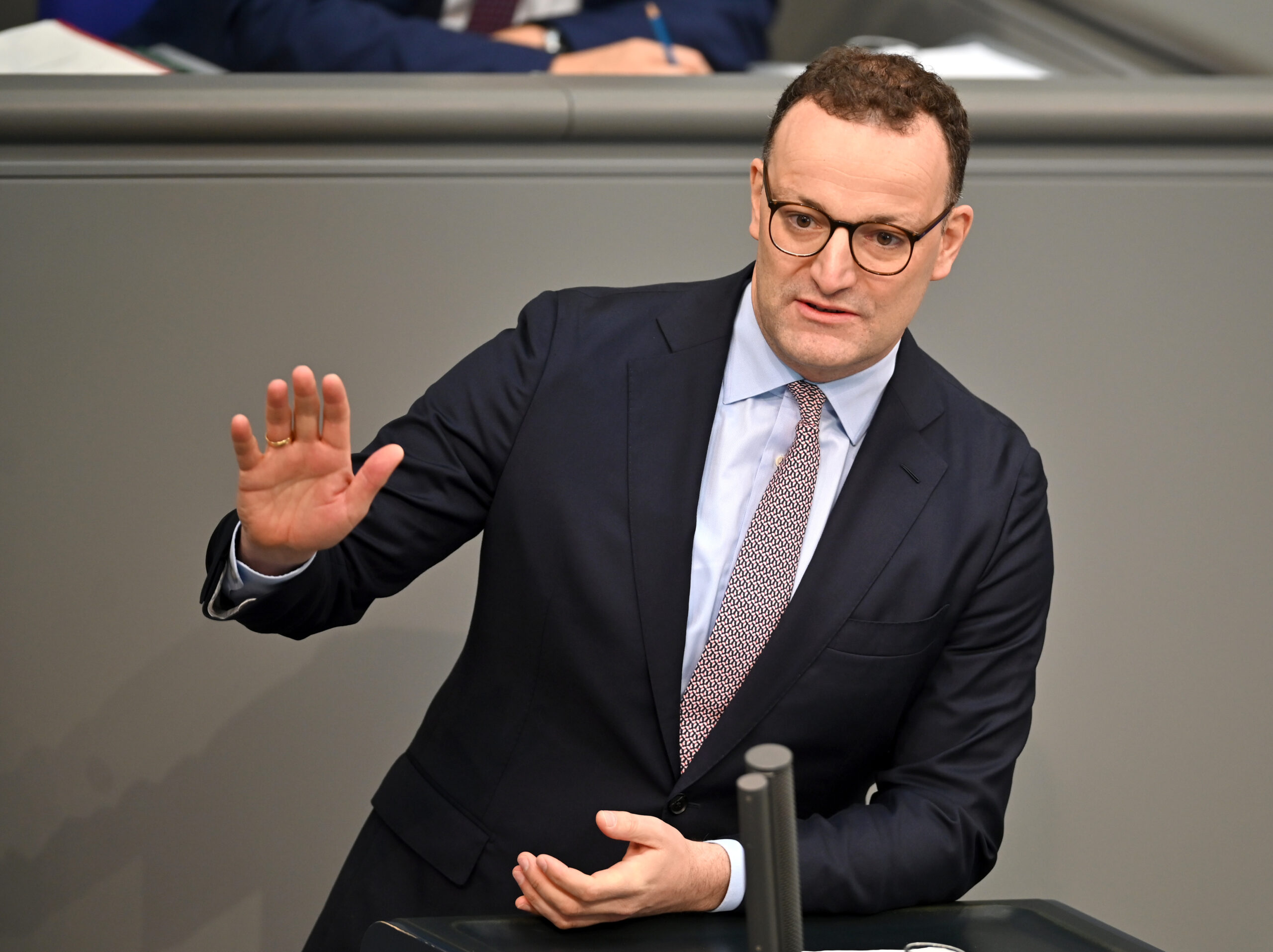 Jens Spahn steht im Anzug im deutschen Bundestag am Mikrofon und hält eine Rede