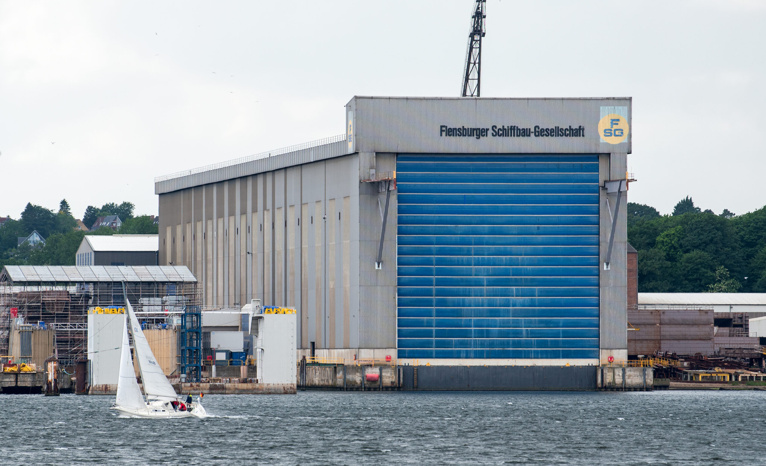 Werfthalle der Flensburger-Schiffsbau-Gesellschaft (FSG). Ein großes graues Gebäude am Wasser mit einem blauen Tor.