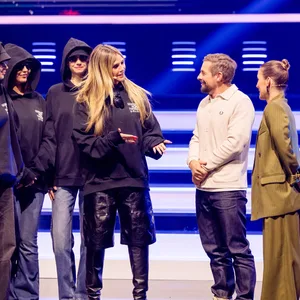 Bei „Joko und Claas – Das Duell um die Welt“ steht Modelmama Heidi Klum, flankiert von mehreren Menschen in Kapuzen-Pullis und mit Sonnenbrille: ihre neuen Models, der kommenden Staffel GNTM