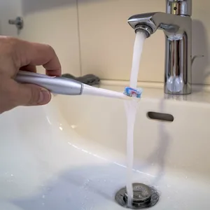 Eine Person hält eine elektrische Zahnbürste unter einen laufenden Wasserhahn im Badezimmer