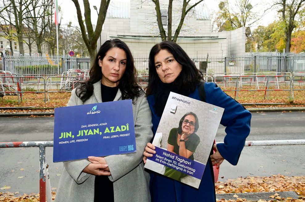 Zwei Frauen mit Plakaten vor einem gesicherten Gebäude