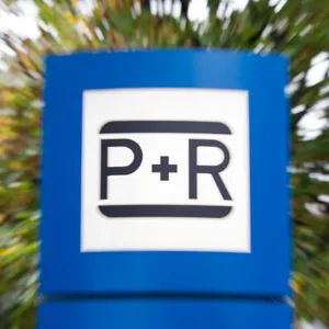 Das Bild zeigt, das blau-weiße Symbol einer Park und Ride Anlage. Im Hintergrund ist ein verschwommener Baum zu sehen