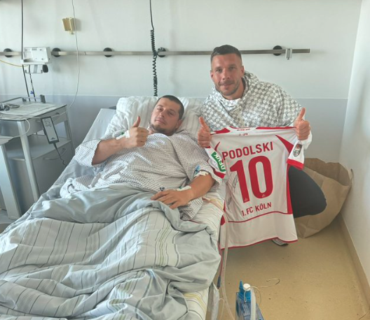 Lukas Podolski am Krankenbett des verletzten Fan