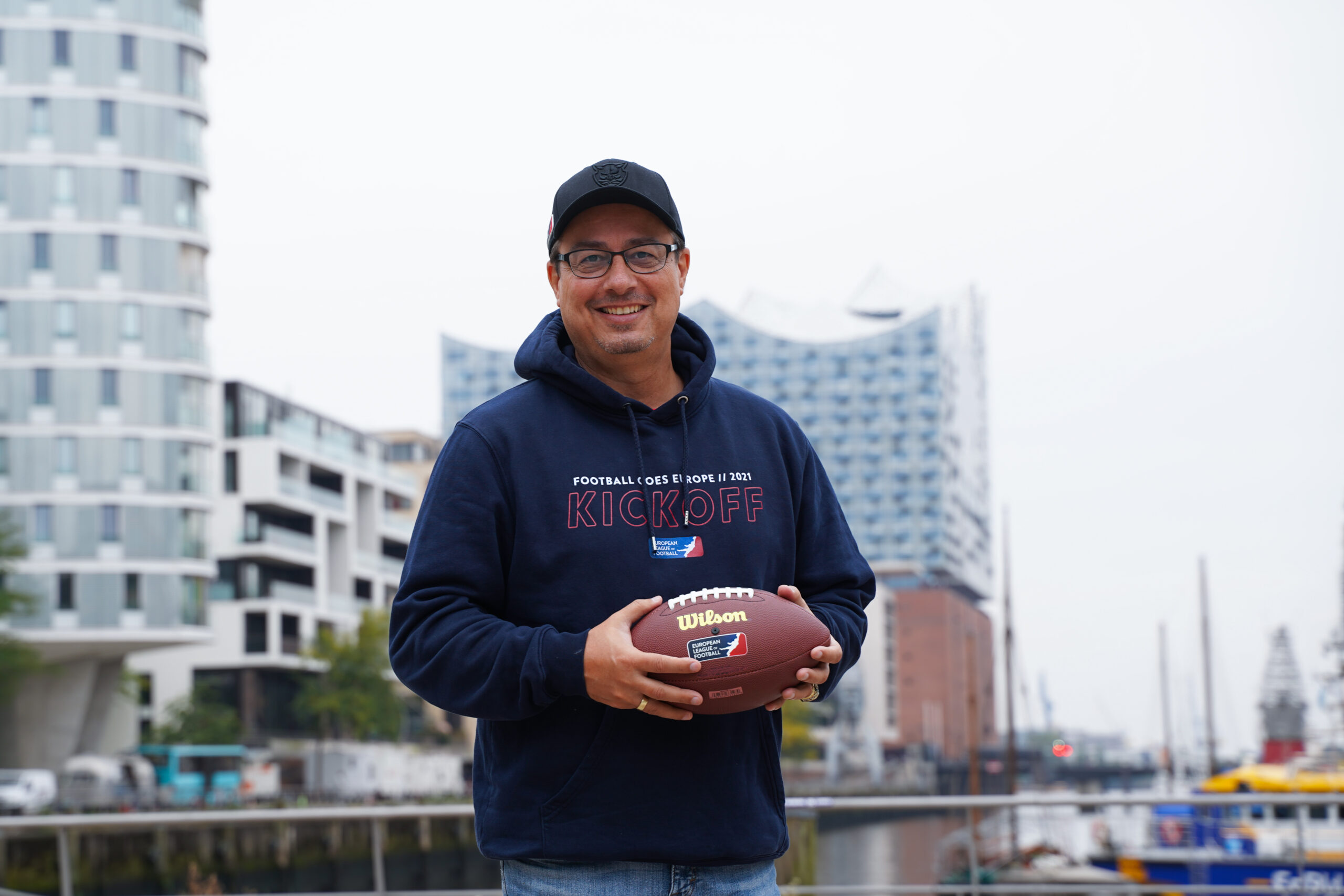 Shuan Fatah hält einen Football vor der Elbphilharmonie