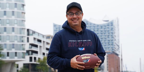 Shuan Fatah hält einen Football vor der Elbphilharmonie