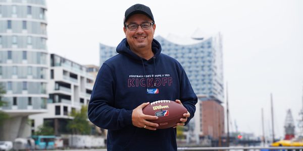 Shuan Fatah hält einen Football vor der Elbphilharmonie