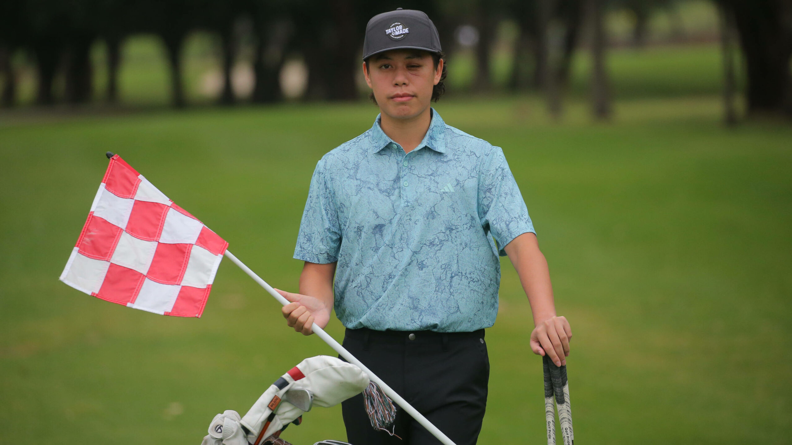 Jeffrey Guan steht in Polohemd auf einem Golfplatz, mit Fahne und Schlägern in der Hand