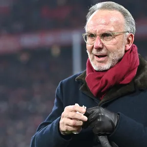Karl-Heinz Rummenigge mit Mantel und Schal in der Allianz Arena hält ein Taschentuch in der Hand