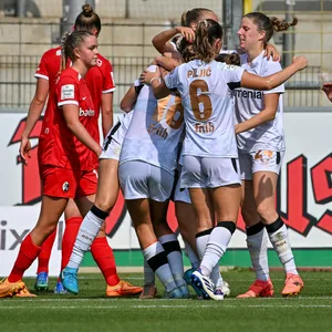 Frauenmannschaft von Bayer Leverkusen steht in einer Jubeltraube beim Spiel gegen den SC Freiburg