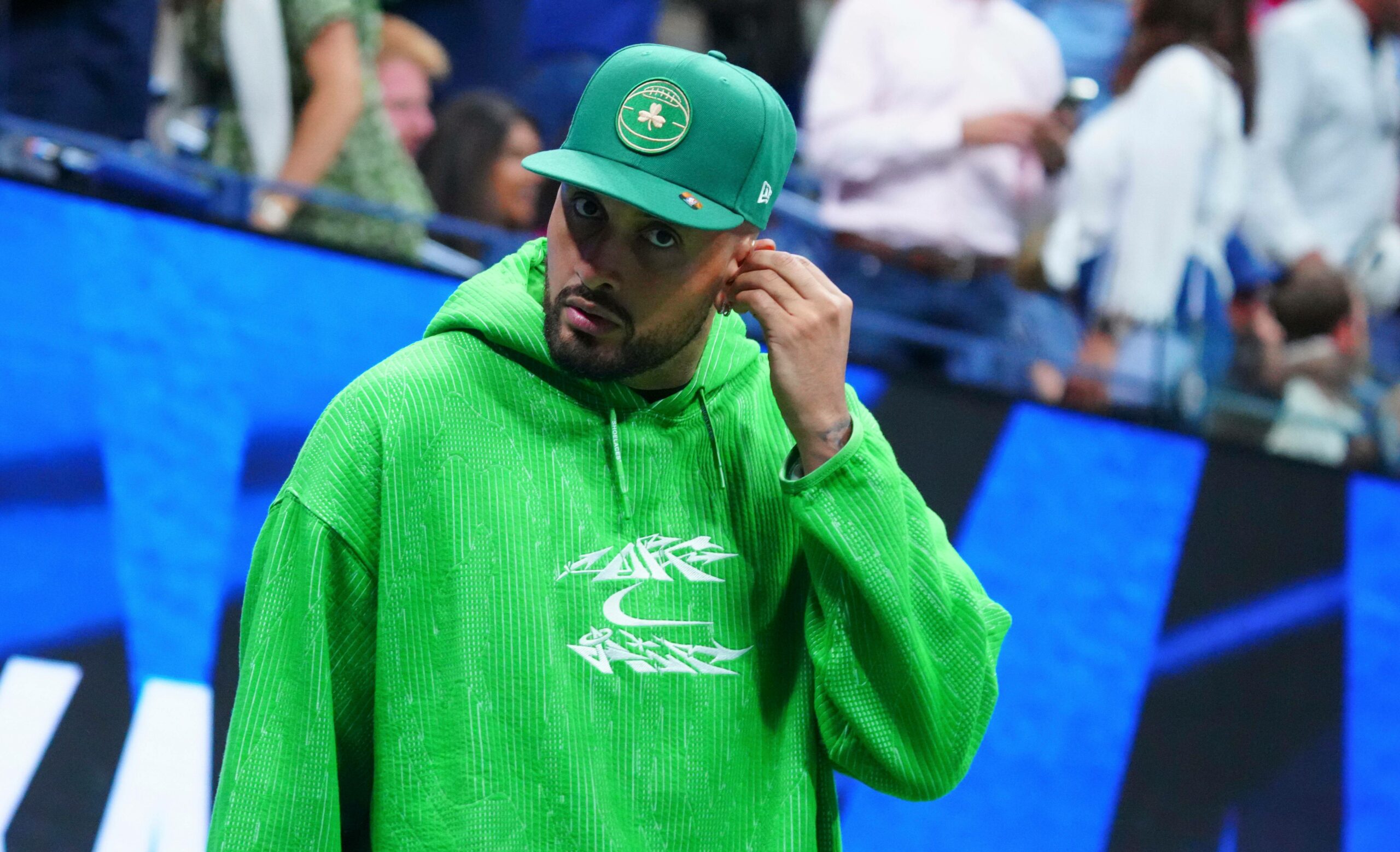 Nick Kyrgios in grünem Sweatshirt, richtet sein Mikrofon am Ohr