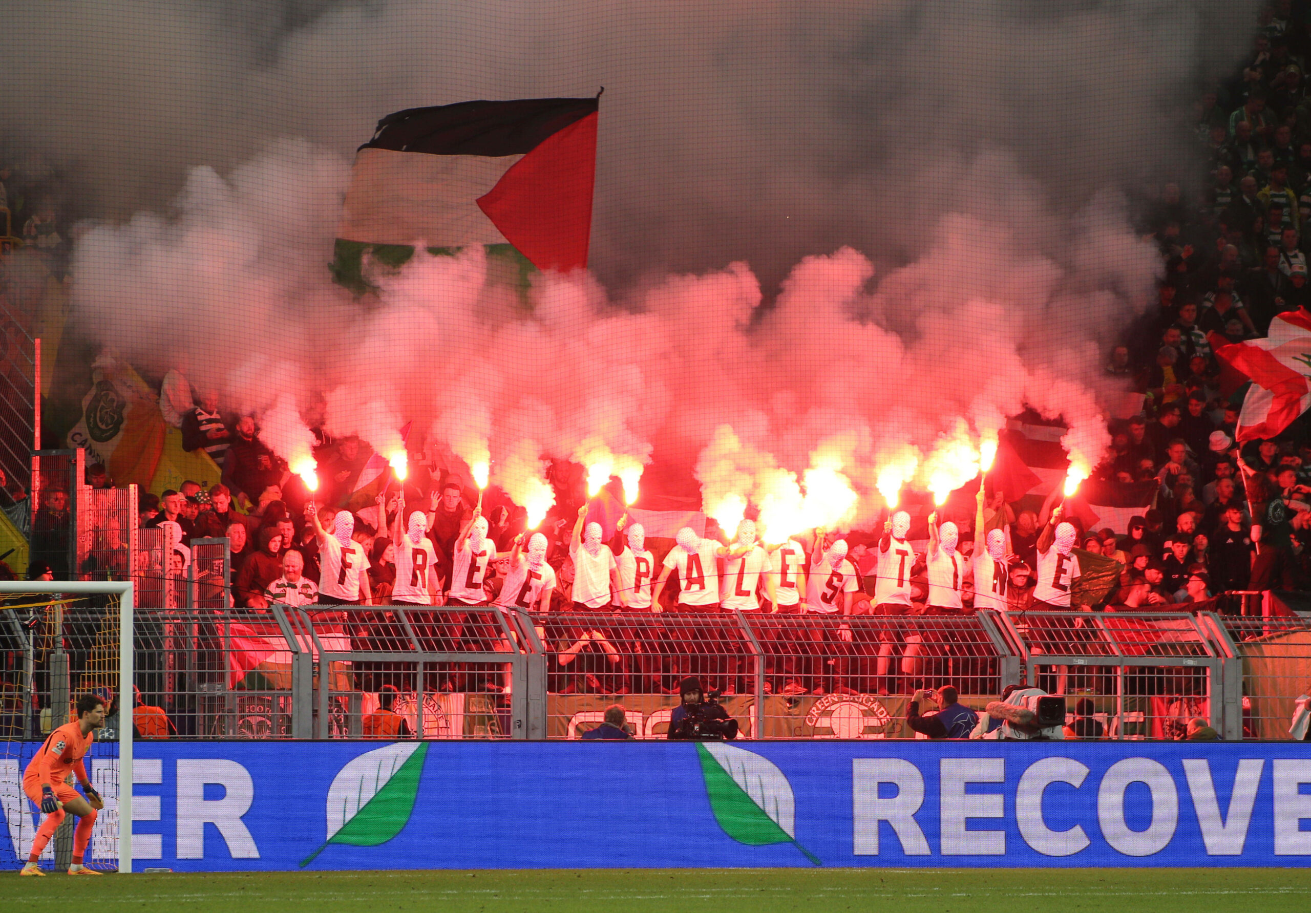 Fans von Celtic Glasgow zünden Pyrotechnik. Die vermummten tragen T-Shirts die zusammen „Free Palestine“ ergeben