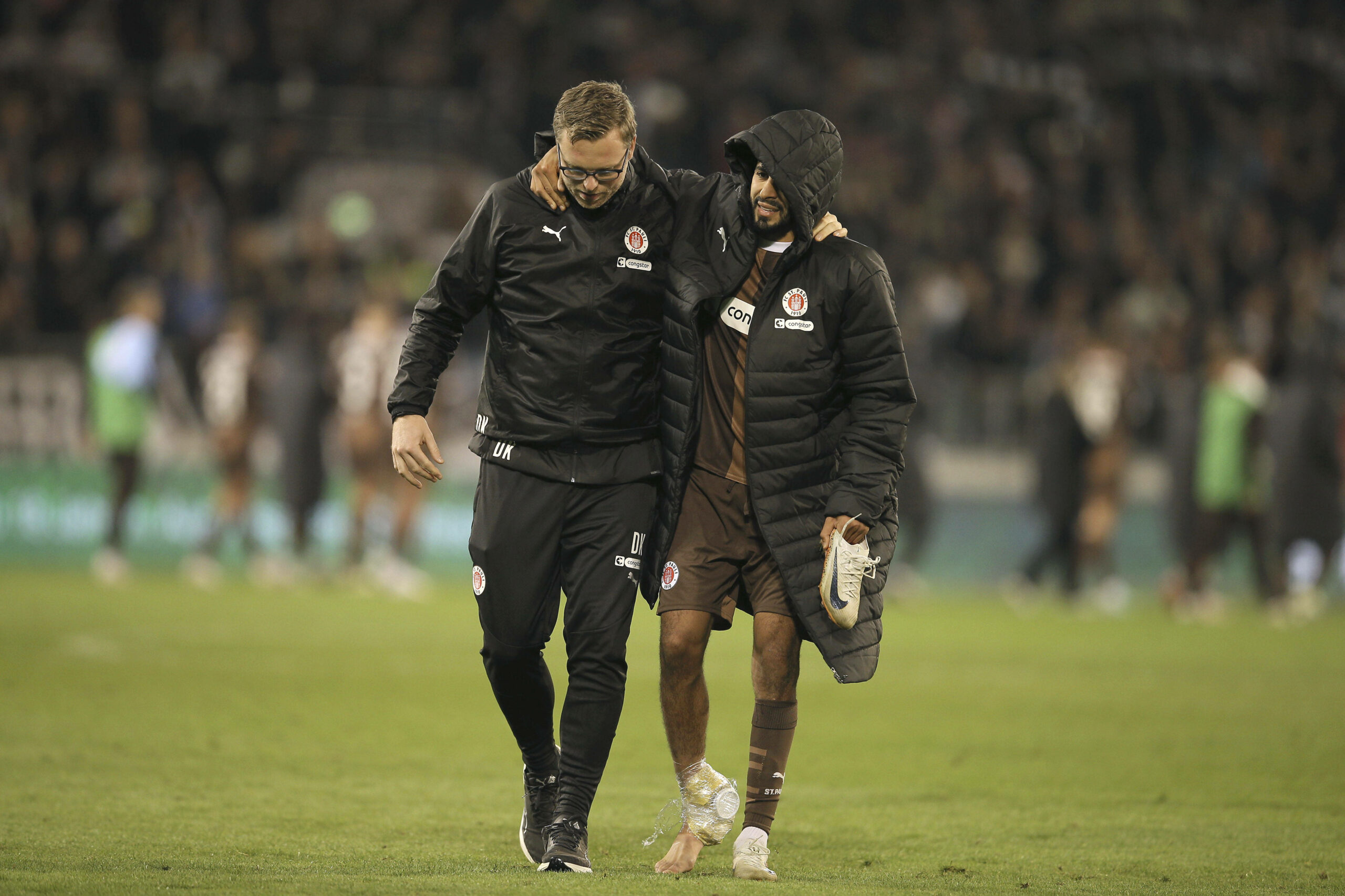 Elias Saad (FC St. Pauli) wird von einem Betreuer gestützt, während er vom Platz geht