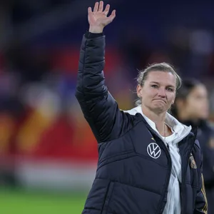 Alexandra Popp in Mantel der Nationalmannschaft winkt und guckt traurig