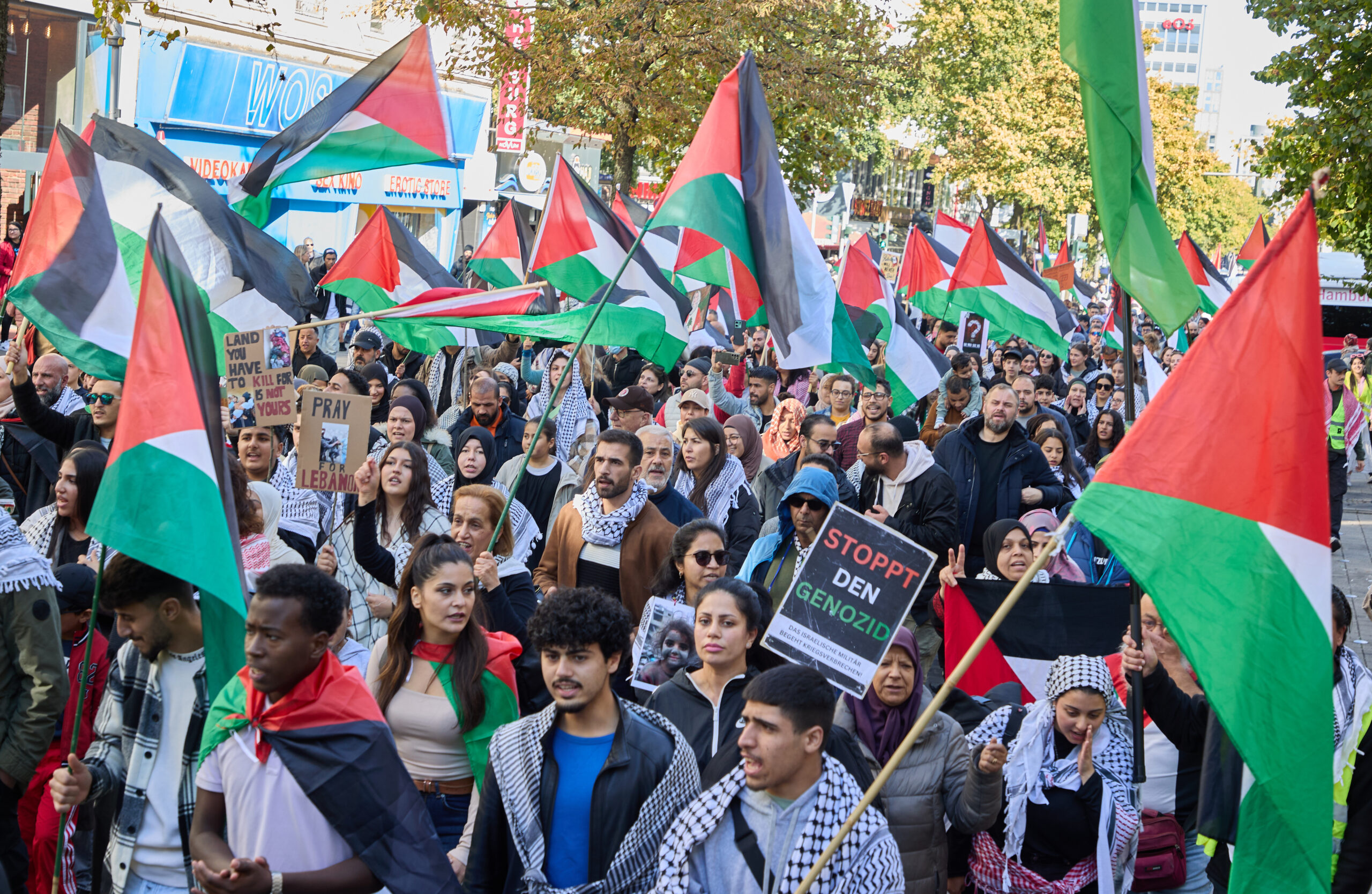 Eine Gruppe von Demonstranten schwenkt palästinensische Flaggen und halten Schilder mit der Aufschrift „Stoppt den Genozid“ in die Höhe.