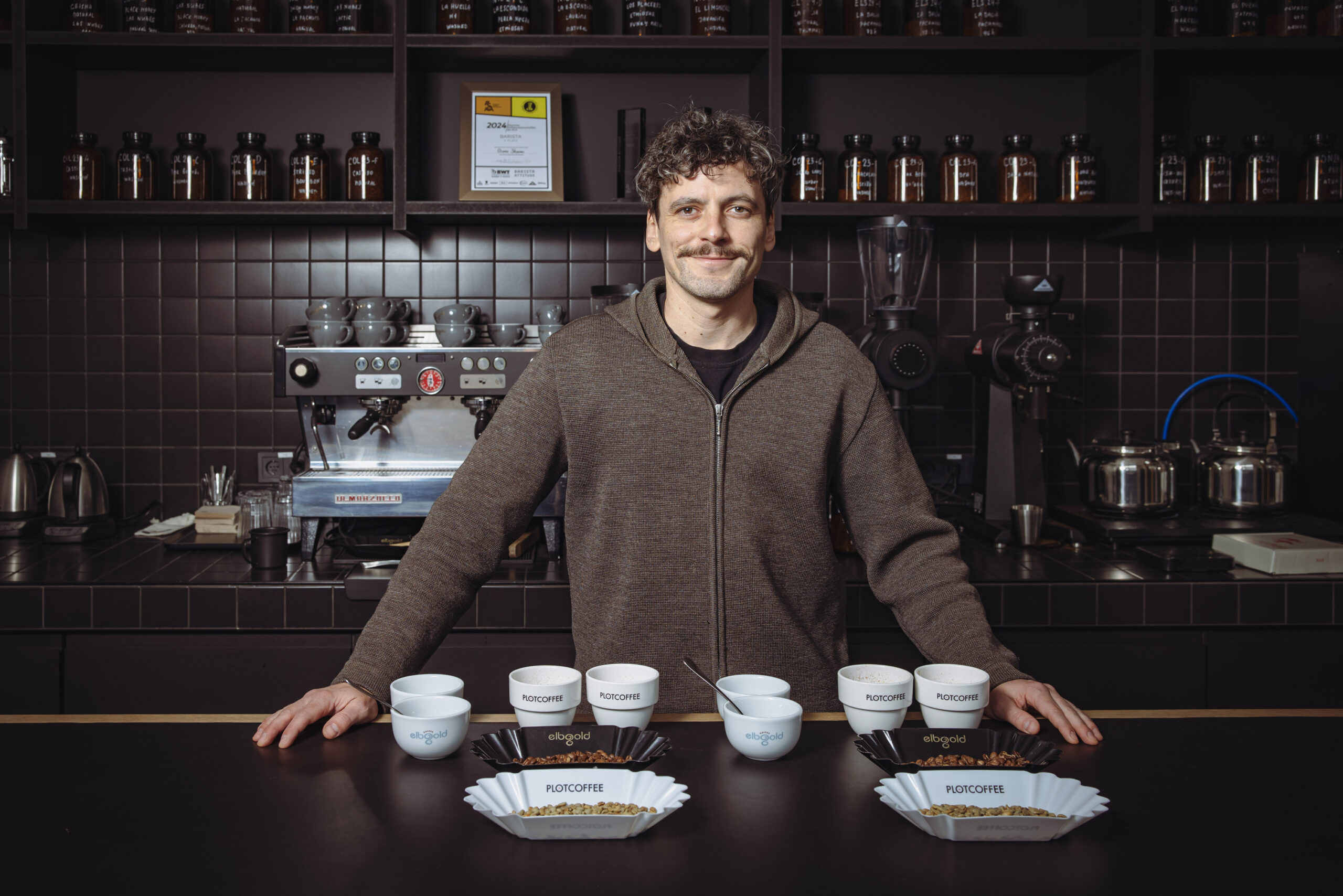 Junger Mann vor Kaffeemaschine mit Kaffeebechern vor sich