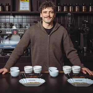 Junger Mann vor Kaffeemaschine mit Kaffeebechern vor sich