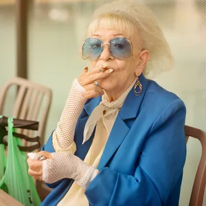 Eine alte Dame in blauem Blazer raucht eine Zigarette.
