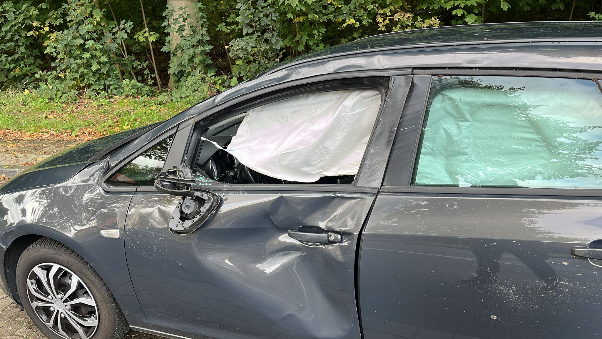 Ein graues Auto mit großen Dellen und ausgelöstem Airbag