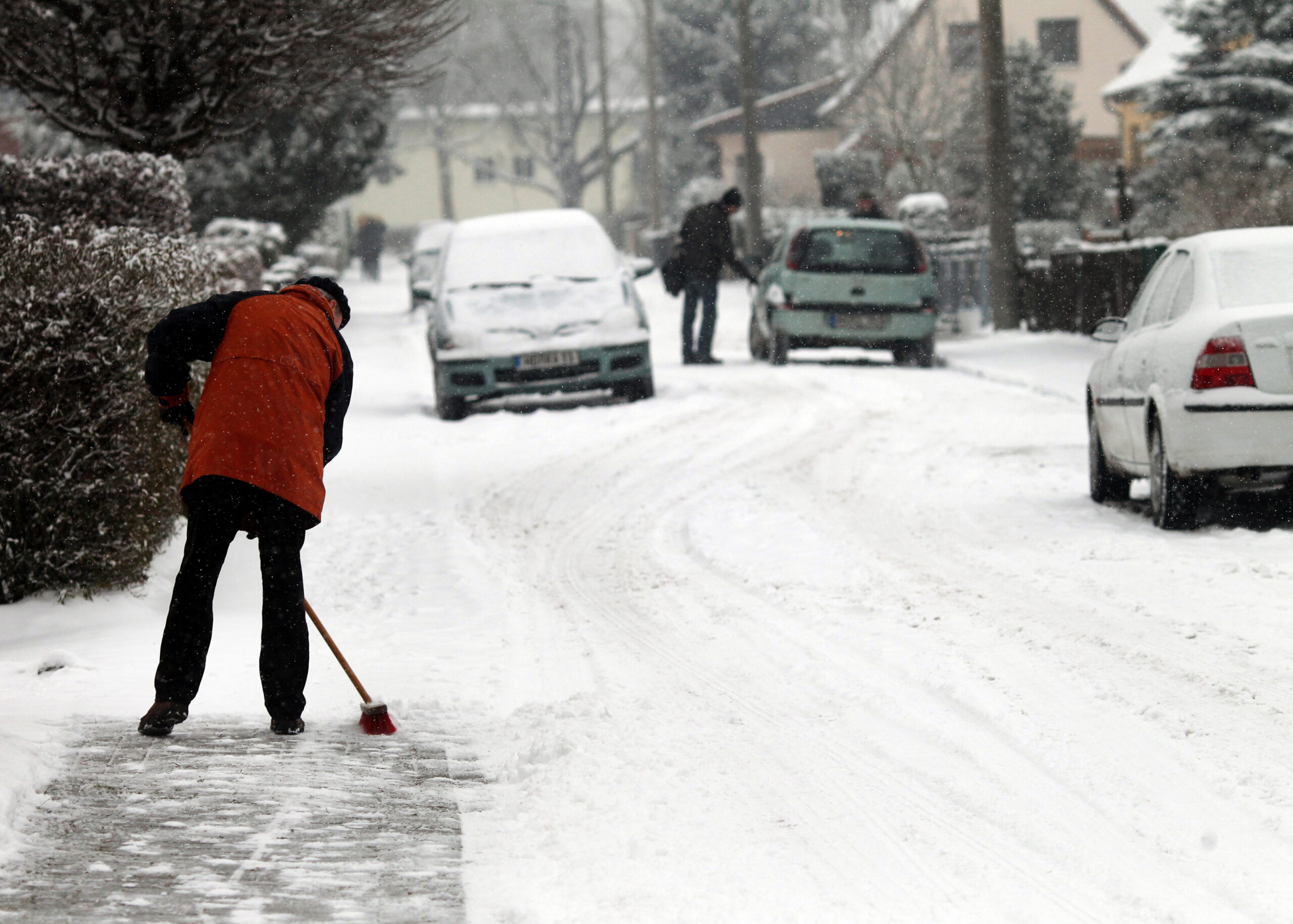 Frau fegt Schnee vom Gehweg