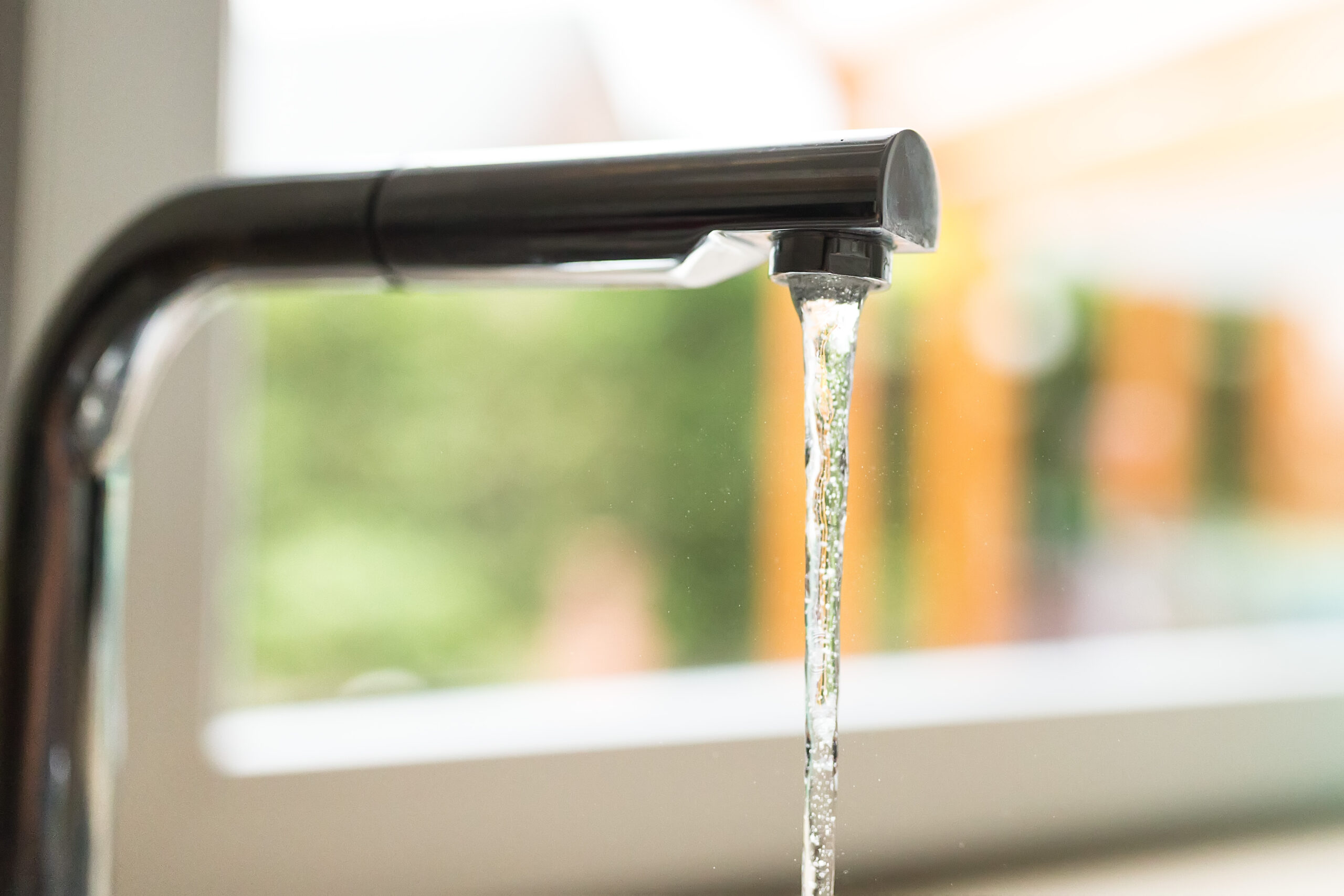 Ein laufender Wasserhahn vor einem Fenster.