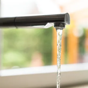 Ein laufender Wasserhahn vor einem Fenster.