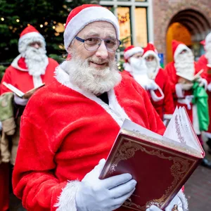 Ein Mann mit rotem Mantel, Kapuze und Bart liest aus einem Buch vor