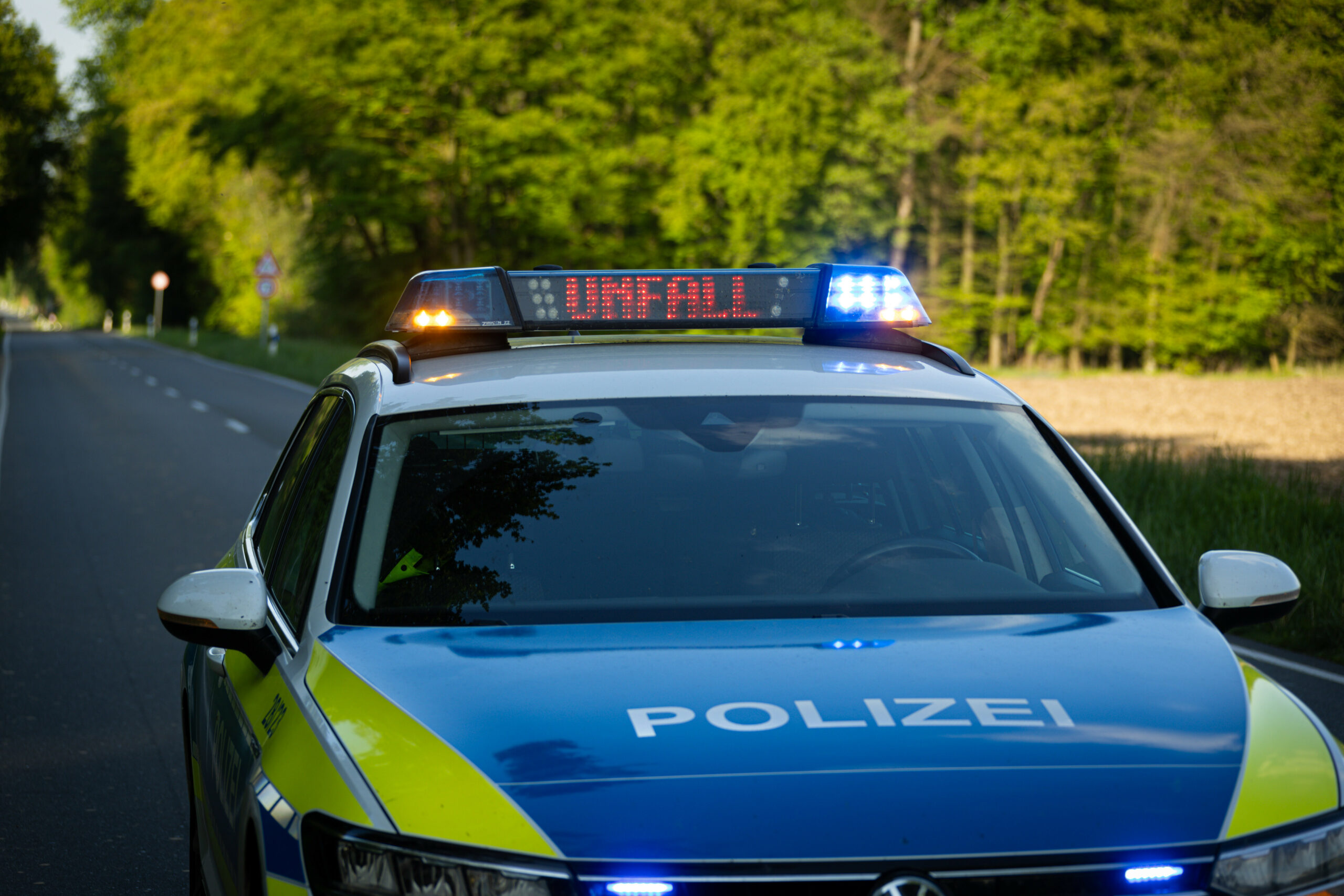 Ein Streifenwagen der Polizei steht mit Blaulicht und dem Schriftzug Unfall im Display an einem Unfallort.