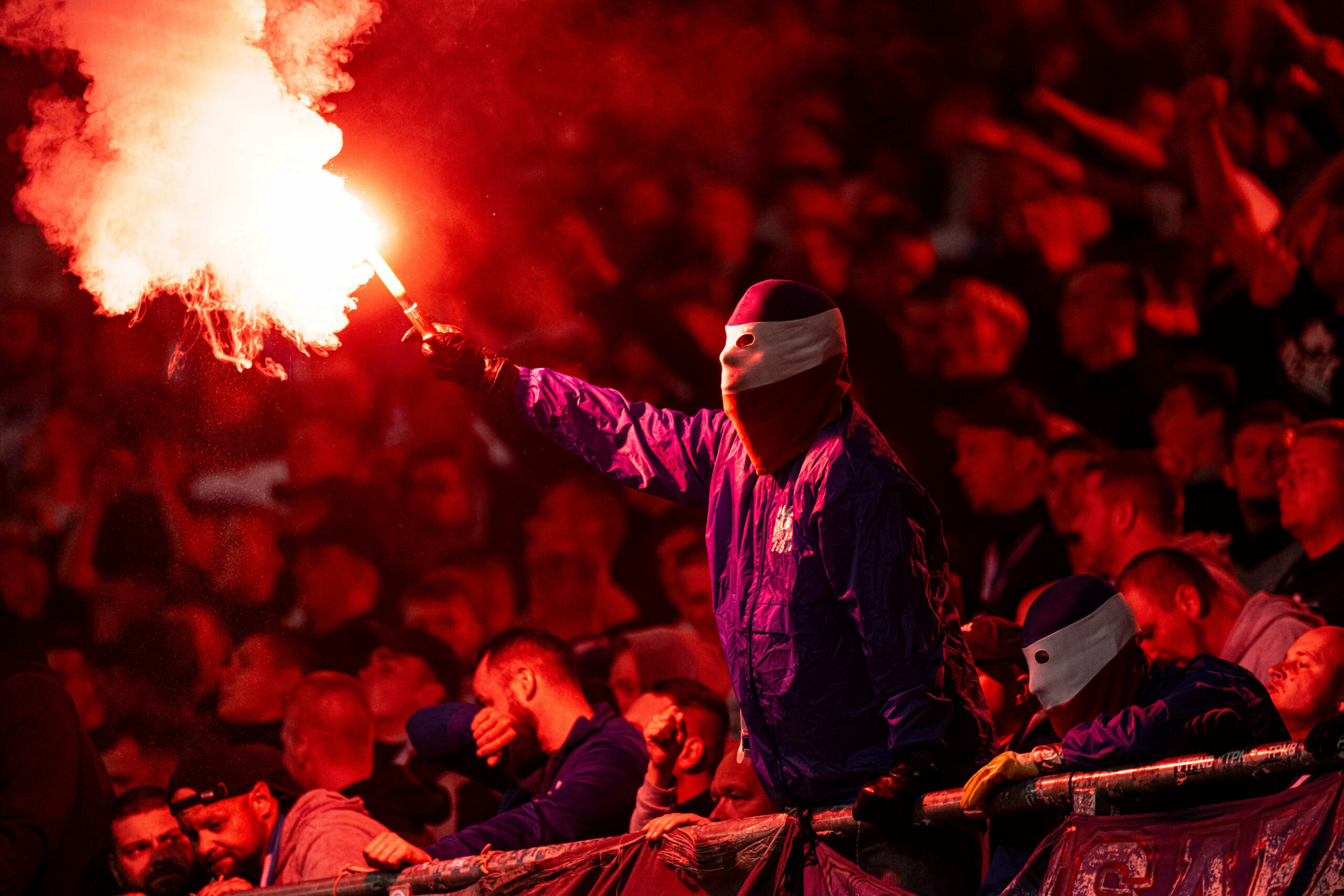 Ein maskierter Ultra von Hansa Rostock zündet Pyrotechnik im Fanblock