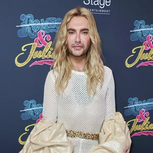 Ein Mann mit langen blonden Haaren in beige-glitzernder Abendgarderobe auf dem roten Teppich