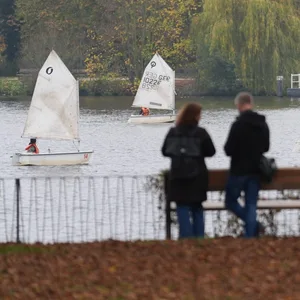 Zwei Menschen spazieren entlang der Außenalster. Im Hintergrund sind Segelboote