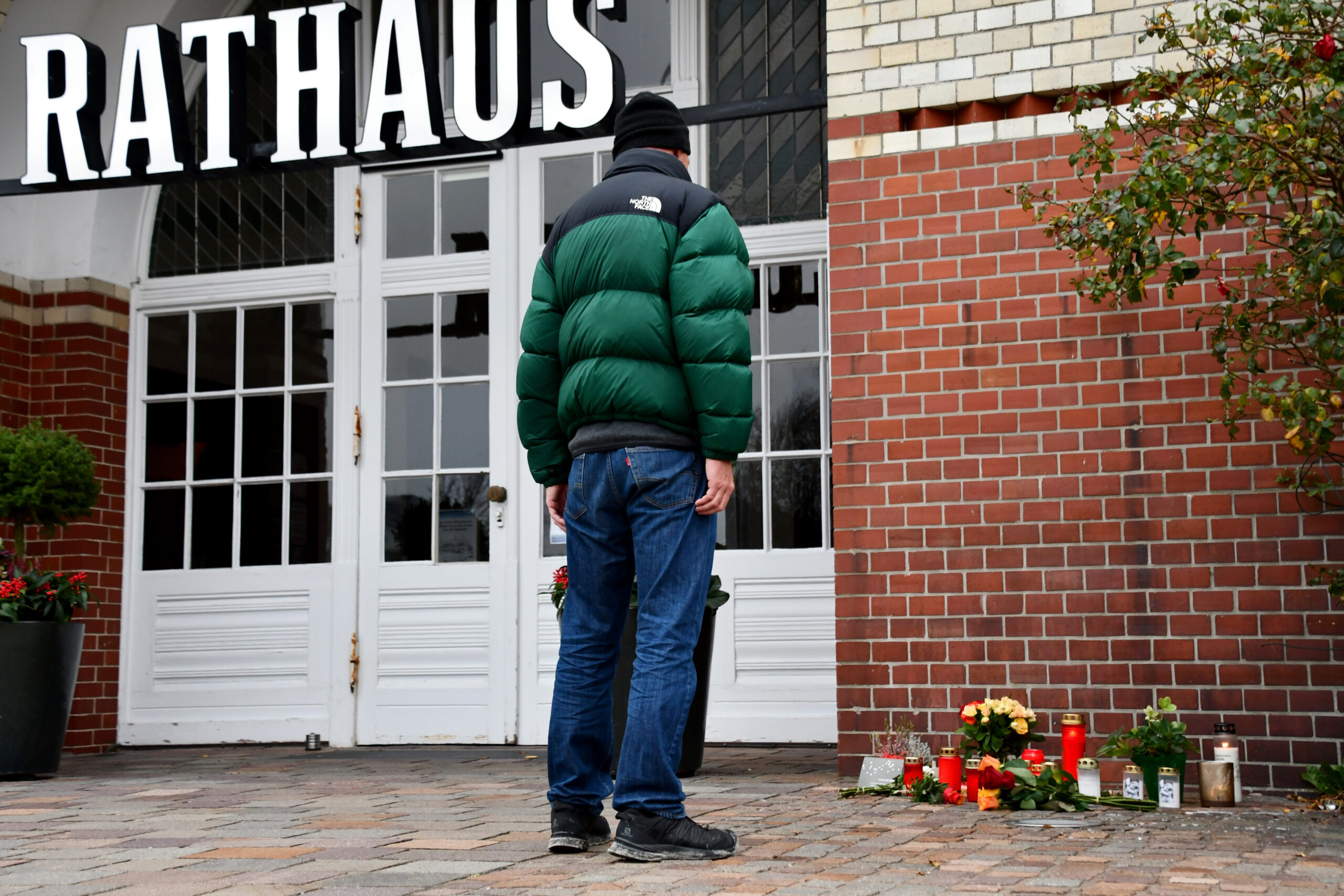 Ein Mann steht vor einem Backsteingebäude vor dem Blumen niedergelegt wurden